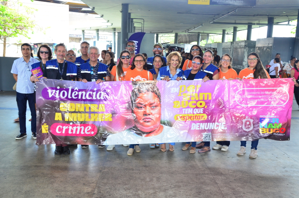 Equipe de educação e fiscalização do Consórcio de Transporte Metropolitano e equipe da Secretaria da Mulher pousando com faixa