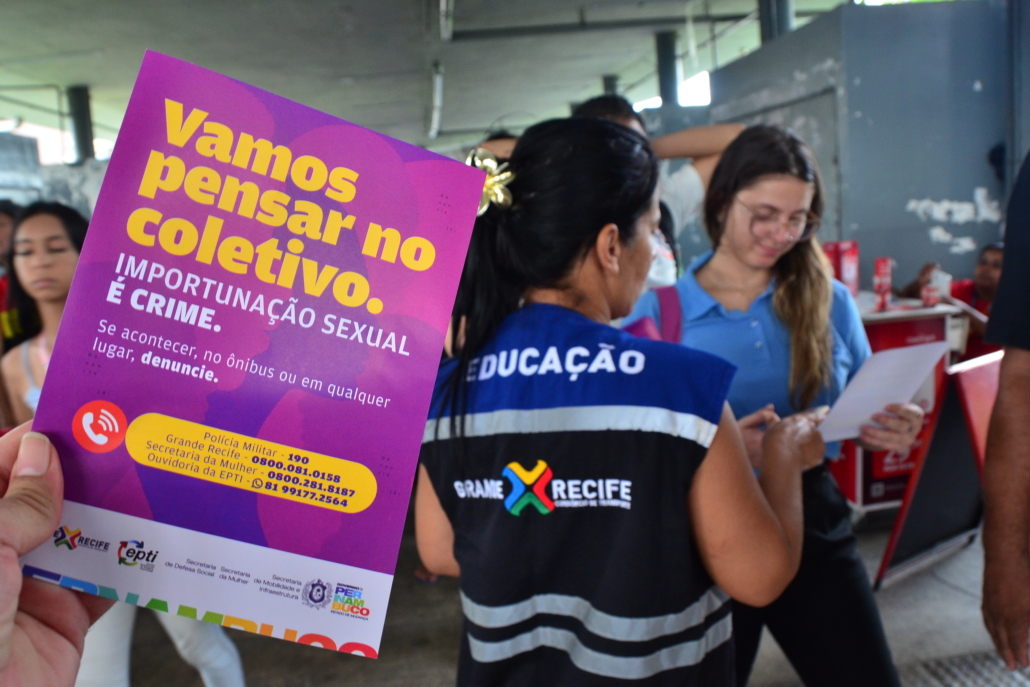 Panfleto contra o assédio sexual nos coletivos. Ao fundo, mulher entregando panfleto para outra mulher