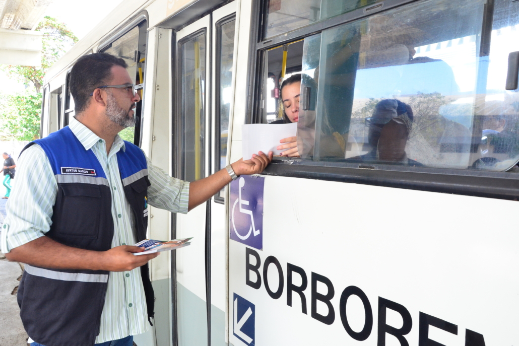 Homem entregando panfleto para um mulher que está sentada sendo do ônibus