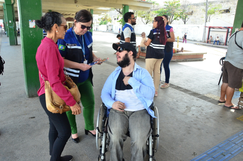 Duas mulheres em pé conversando com um homem cadeirante