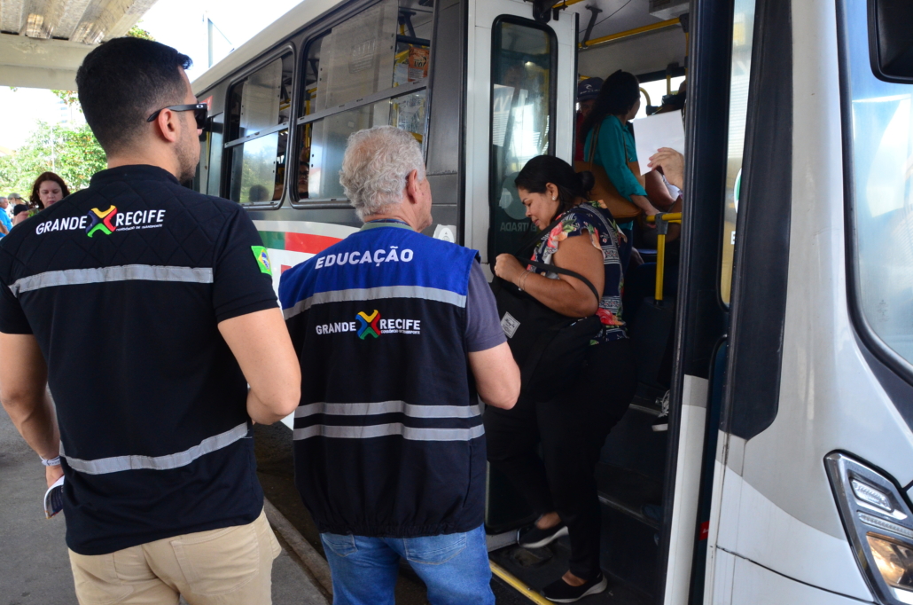 Dois homens em pé na frente da porta dianteira do ônibus. 