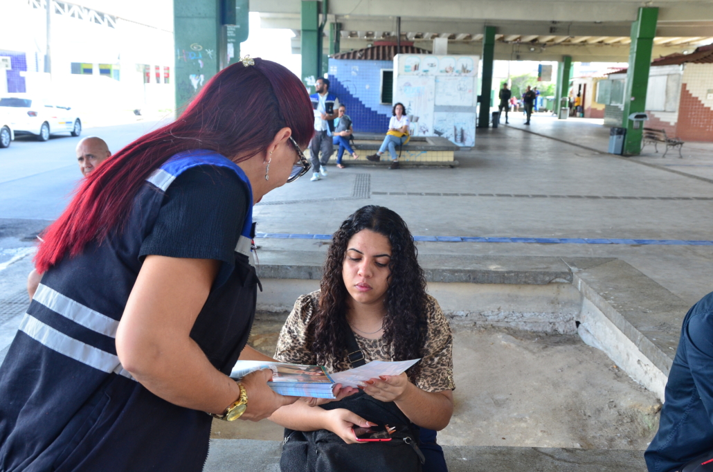 Mulher sentada recebendo um panfleto de um outra mulher