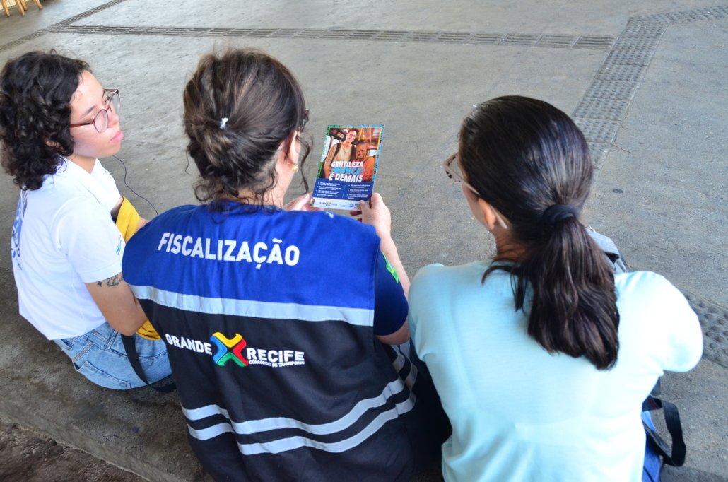 três mulheres sentadas, a do meio está segurando um panfleto