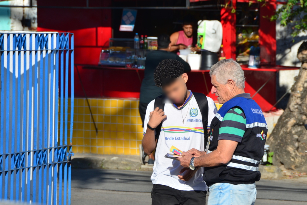 Homem entregando panfleto para aluno de escola estadual