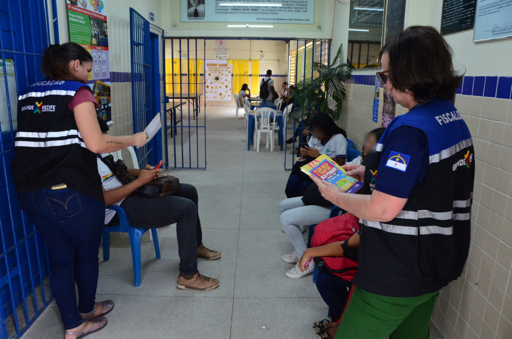 Duas mulheres realizando panfletagem e conversa com alunas e alunos de escola estadual
