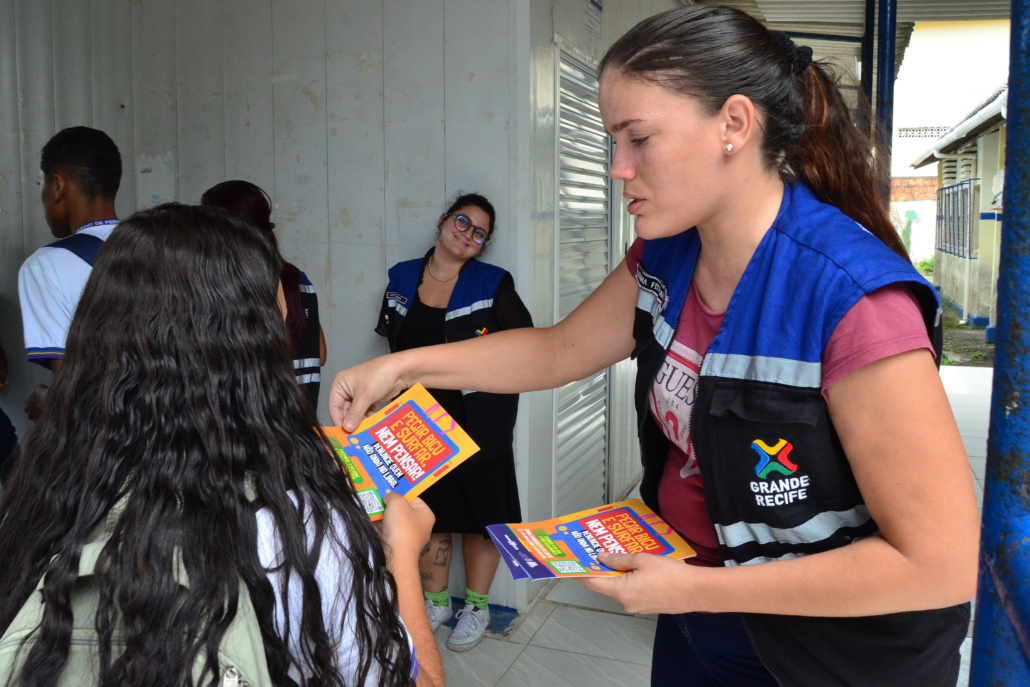 Mulher entregando panfleto para estudante de escola estadual