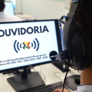 Mulher com fone de ouvido olhando para tela de computador com o nome "OUVIDORIA" na tela.