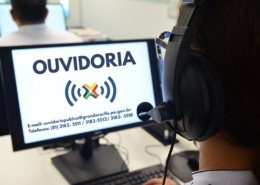 Mulher com fone de ouvido olhando para tela de computador com o nome "OUVIDORIA" na tela.