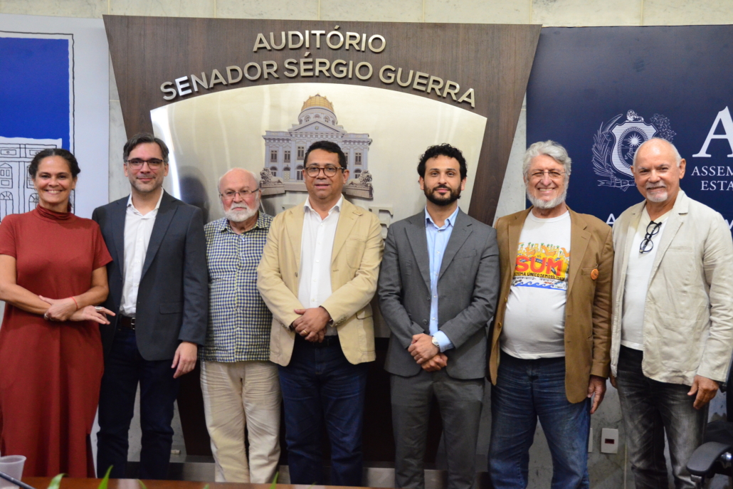 Sete pessoas pousando para foto, da esquerda para direita, uma mulher e seis homens. 