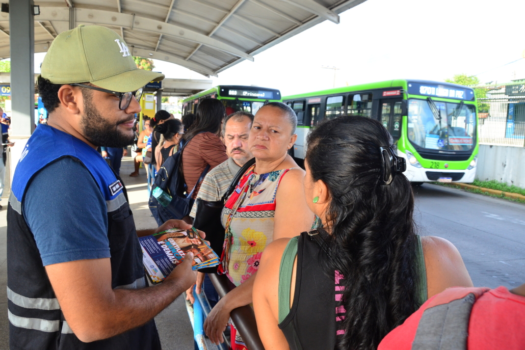 Homem conversando e entregando panfleto para mulheres que estão na fila do ônibus