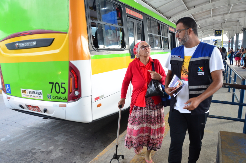 Homem conversando com mulher idosa. Ao fundo, ônibus