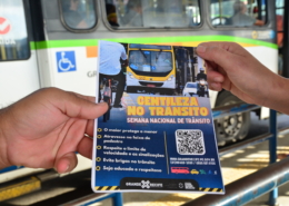 Duas mãos segurando um panfleto e ao fundo u ônibus